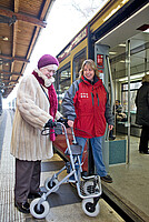 Der Begleitservice unterstützt eine Kundin mit einem Rollator beim Einstieg in den Zug